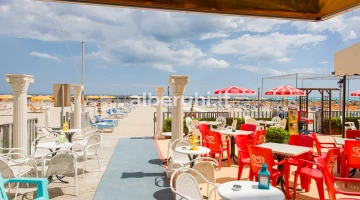 Die Terrasse (mit Tischen und Stühlen) auf dem Sand und dem Meer